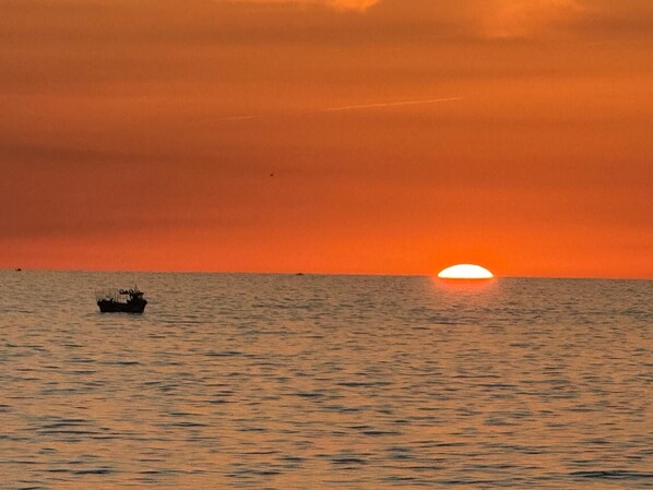 Un coucher de soleil sur une mer calme, avec un bateau à l'horizon.
