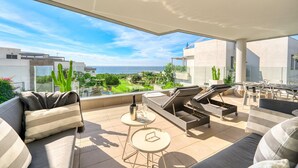 A modern outdoor living area with a sofa, lounge chairs, and a table, overlooking a scenic landscape with buildings and greenery.