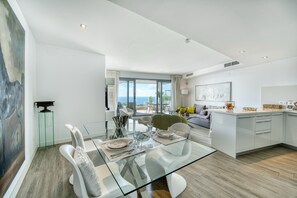 A modern dining area with a glass table, white chairs, and a view of the sea. - 3070 Luxury Apartment in Terrazas de Marbella, Cabopino (Marbella)