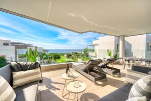 Un espace de vie extérieur moderne, doté d’un canapé, de fauteuils et d’une table, offrant une vue imprenable sur un paysage pittoresque, avec des bâtiments et de la verdure.