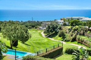A golf course with a swimming pool, surrounded by lush greenery and a view of the sea. - 3070 Luxury Apartment in Terrazas de Marbella, Cabopino (Marbella)