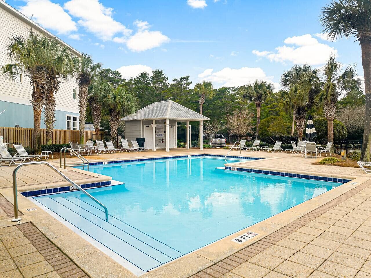 A rectangular swimming pool with a tiled edge, surrounded by lounge chairs and a gazebo.