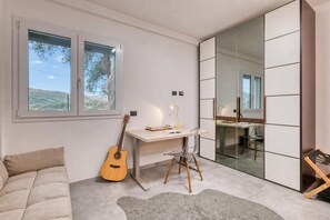 Een moderne kamer met een bureau, een gitaar, een stoel, een bank en een grote spiegel.