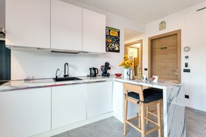 Una cocina moderna con armarios blancos, encimera de mármol, cafetera y puerta de madera.