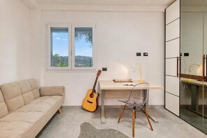 Una habitación moderna con un sofá, un escritorio con una guitarra, una alfombra pequeña y vistas al exterior a través de una ventana.