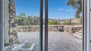Blick durch eine Glastür auf eine Steinmauer und eine Schotterterrasse.