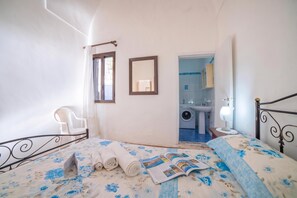 A bedroom with a bed, a chair, a mirror, and a view of a bathroom.