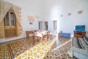 A dining area with a table set for four, a television on a stand, and a patterned floor. - Marisole House With Sea View, Santa Cesarea Terme, Italy (Santa Cesarea Terme)