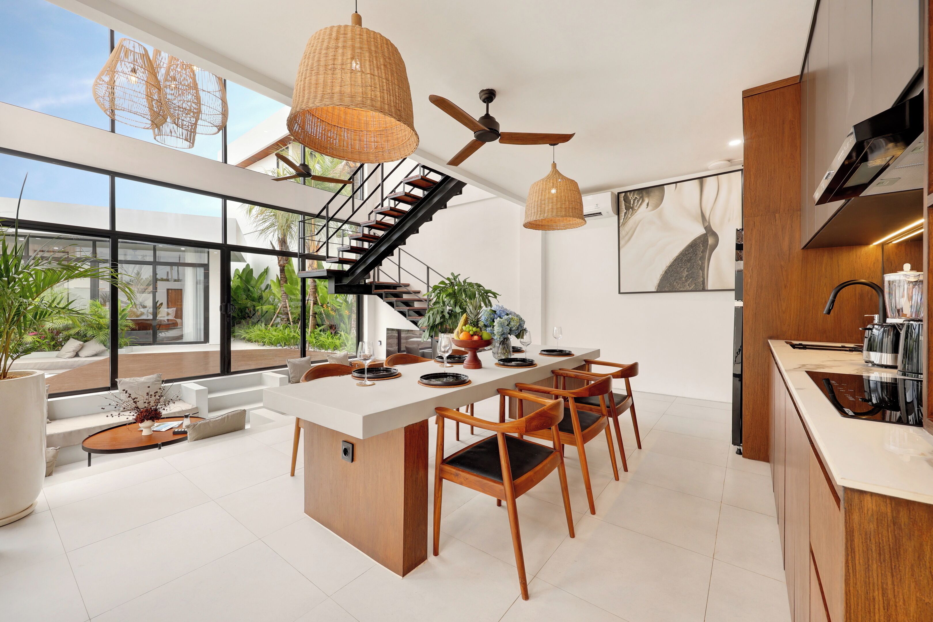 A modern kitchen with a central island, wooden chairs, and a staircase leading to an upper level.