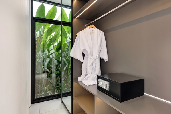 A modern bathroom with a glass door leading to a balcony, a white robe hanging on a wooden hanger, and a black electronic device on a shelf. - Baliwood Residence Villas II (Munggu)