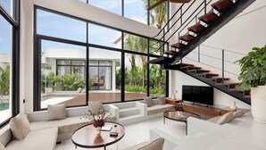 Un salon moderne doté de grandes fenêtres, d’un escalier et d’un téléviseur.