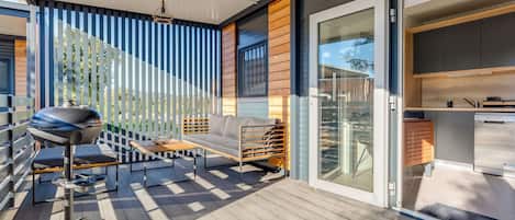 A modern outdoor patio with a grill, seating, and a view of the backyard.