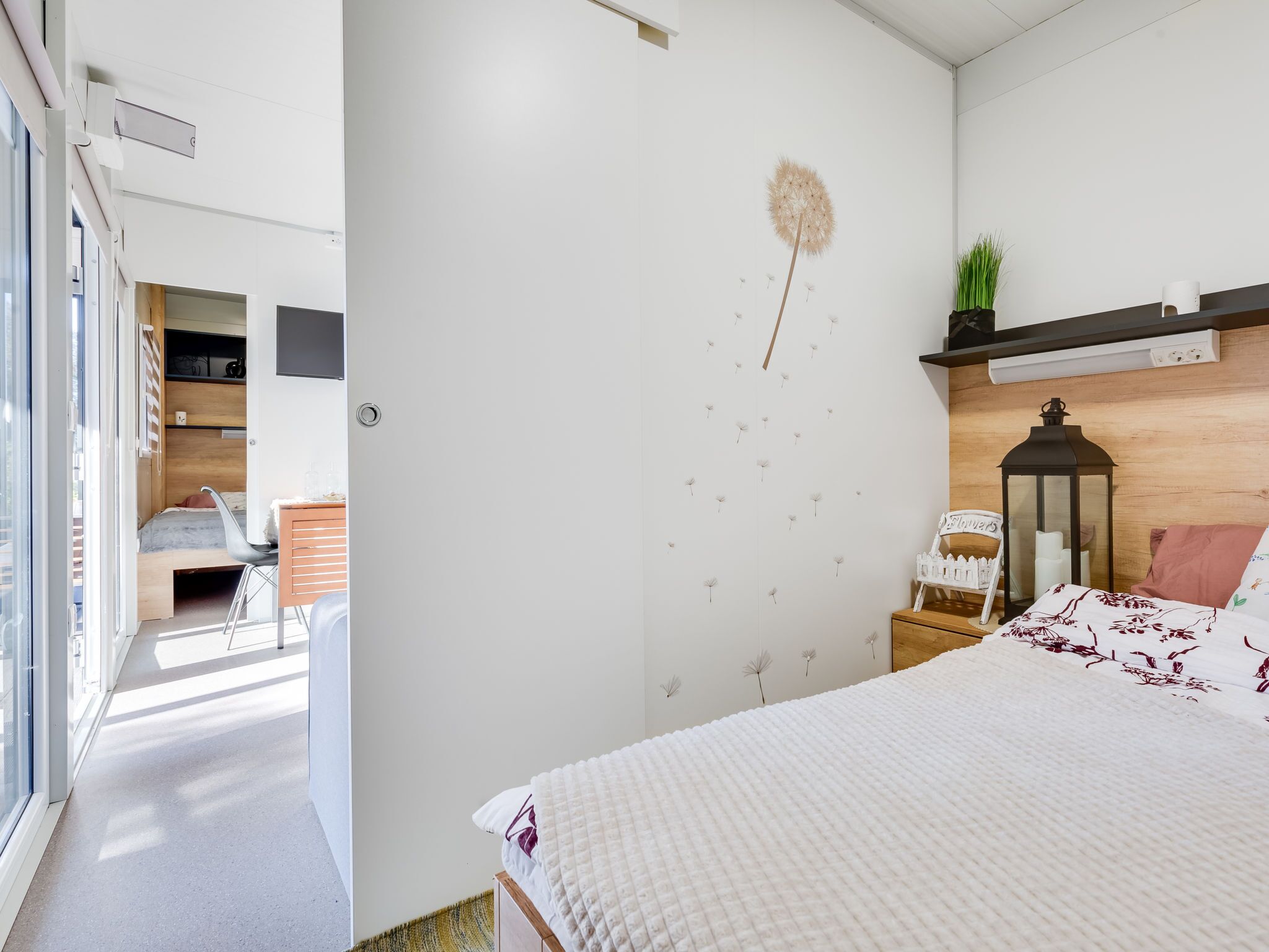 Un dormitori modern amb un llit gran, una tauleta de nit, una estanteria penjada amb una planta, i un llorer decoratiu a la paret.