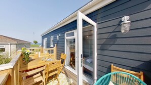 A deck with wooden furniture, a glass door, and a small outdoor area with a chair. - D46 Wrangarrie, Riviere Towans (Hayle)