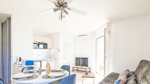 A modern living room with a grey sofa, a dining table with chairs, a TV, and a ceiling fan. - Les Rives Latines by Interhome (Fréjus)