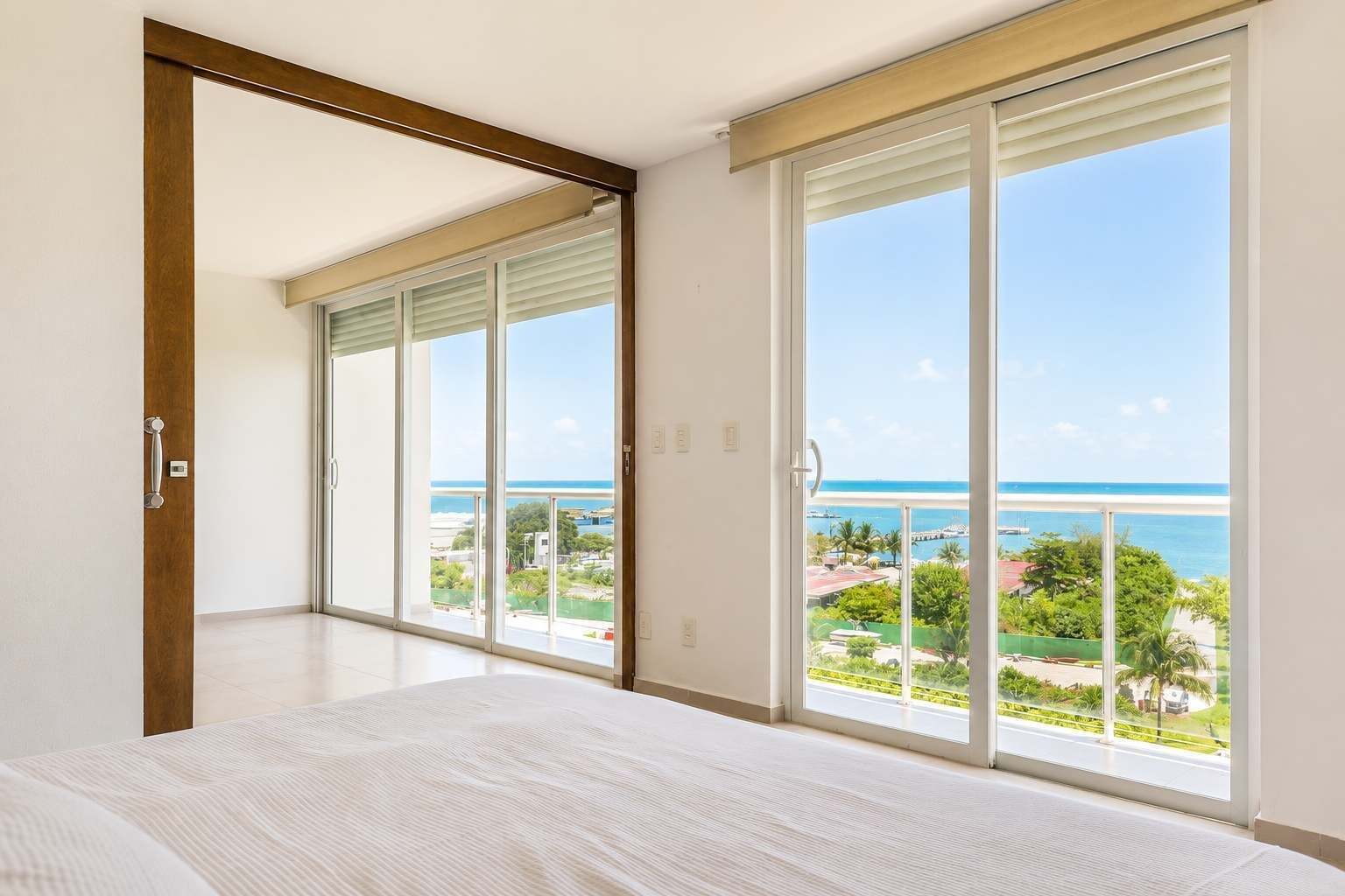 A bedroom with a large bed, sliding glass doors leading to a balcony with a view of the ocean.