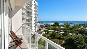 A balcony with a view of a hotel building, a pool area, and the ocean. - Beachfront 3BR - Ocean View - 70m Pool - Cancun (Cancún)