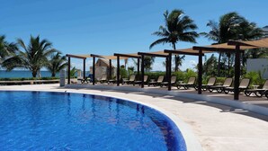 A poolside area with lounge chairs and umbrellas, overlooking a body of water. - Beachfront 3BR - Ocean View - 70m Pool - Cancun (Cancún)