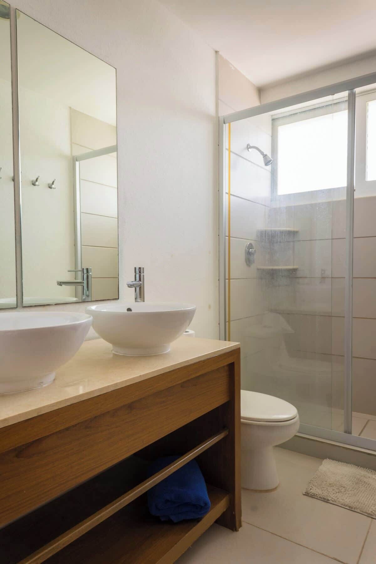 A modern bathroom with a large mirror, two vessel sinks, a toilet, and a glass-enclosed shower.