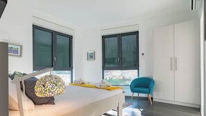 A modern bedroom with a bed, two windows, a wardrobe, and a blue chair.