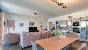 A modern kitchen with stainless steel appliances, a dining area with a table and chairs, and a living area with a sofa and television.