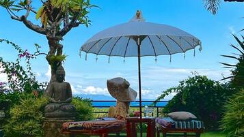 Un espacio al aire libre tranquilo con una sombrilla grande, una estatua de Buda y abundante vegetación.