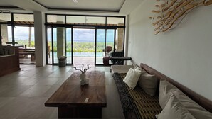 Ein geräumiger Wohnbereich mit Couch, Holztisch und Meerblick durch große Schiebetüren.