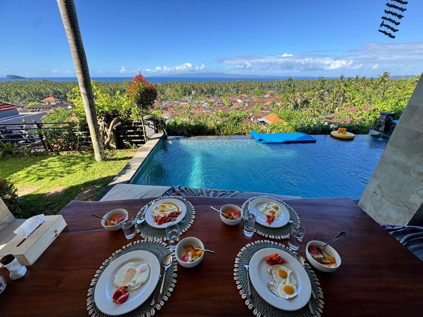 Una mesa de comedor con platos de desayuno, vasos y vistas a la piscina.