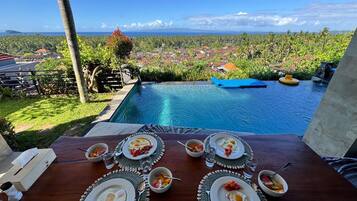 Una mesa de comedor con platos de desayuno, vasos y vistas a la piscina.