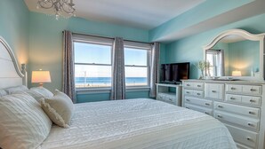 Un dormitorio con una cama grande, un aparador, un televisor y vista a la playa.