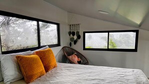 Une chambre à coucher avec un lit, deux fenêtres et une chaise.