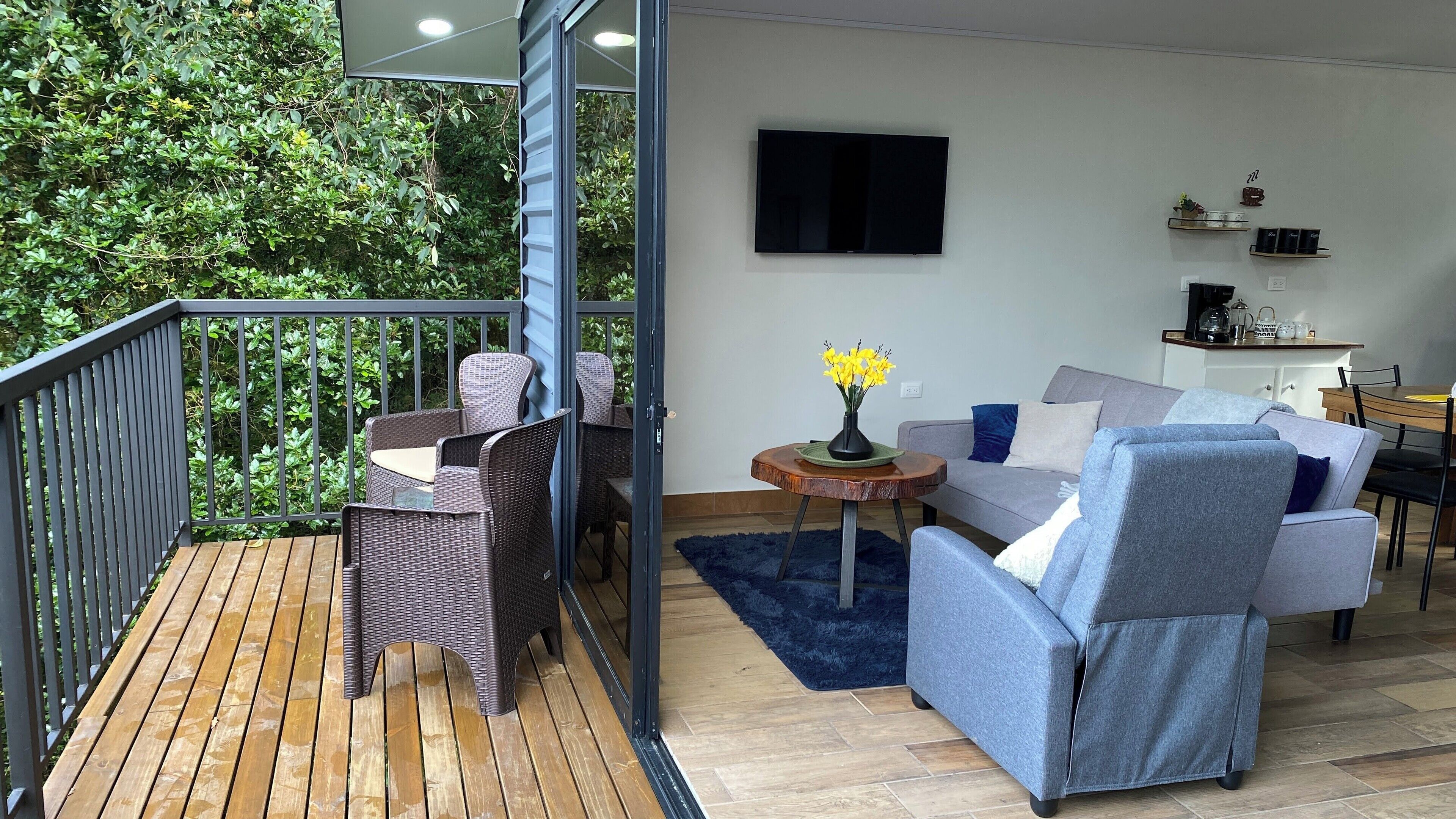 A balcony with wicker furniture, a grey sofa, and a small table with a vase of flowers.