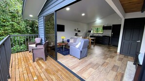Un vaste espace de vie comprenant une terrasse en bois, un ensemble de canapés, une table à manger et un coin cuisine.
