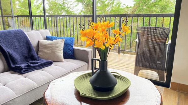 A balcony with a sofa, a chair, and a vase with yellow flowers.