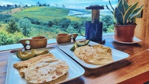 Ein Esstisch mit zwei angerichteten Tellern, darunter Avocado-Scheiben und ein Fladenbrot, sowie zwei Tassen Kaffee.