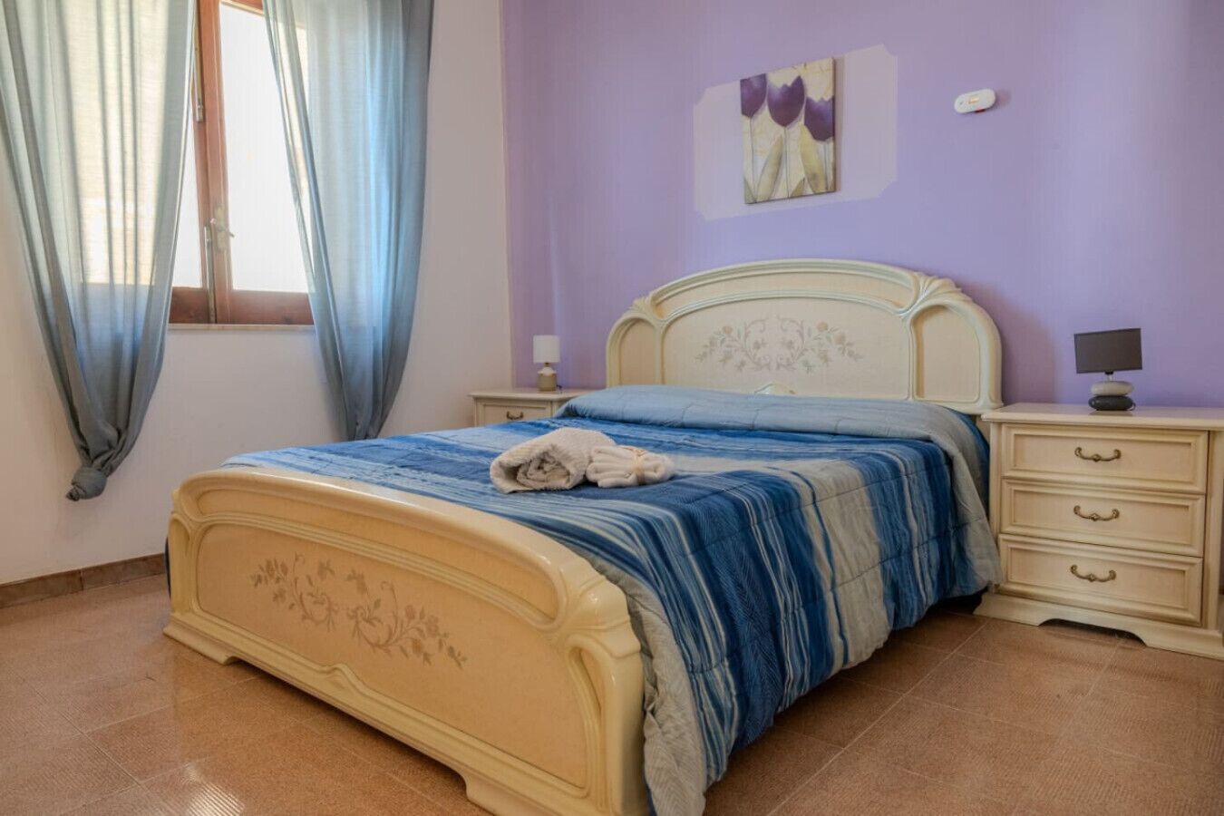 Une chambre à coucher comprenant un lit, une table de chevet, une commode et une fenêtre avec des rideaux.