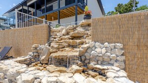 A stone waterfall feature in front of a modern building with a balcony. - 180° Table Rock Lake View | 2-Min to SDC | Kayaks (Branson)