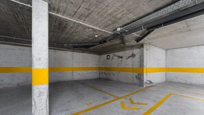 An empty parking garage with concrete walls and yellow lines marking parking spaces. - GuestReady - A dream stay in Porto (Porto)