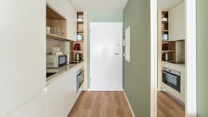 A narrow kitchen with built-in appliances, wooden shelves, and a white door. - GuestReady - A dream stay in Porto (Porto)