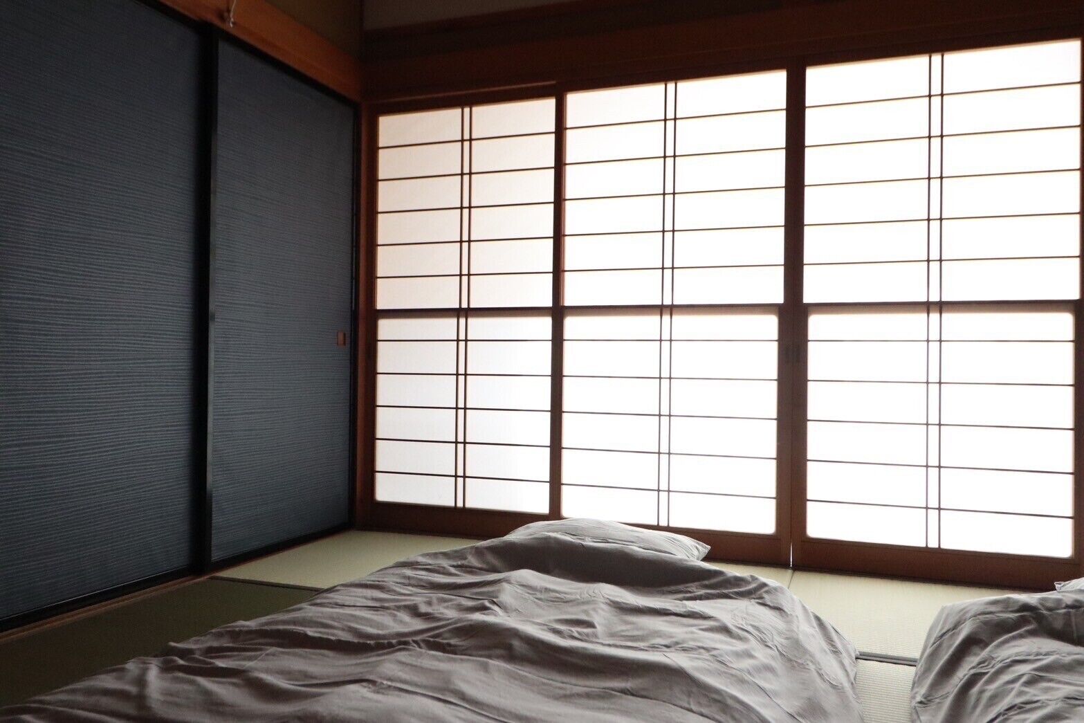 A room with tatami mat flooring, a sliding shoji screen door, and a bed with white bedding.