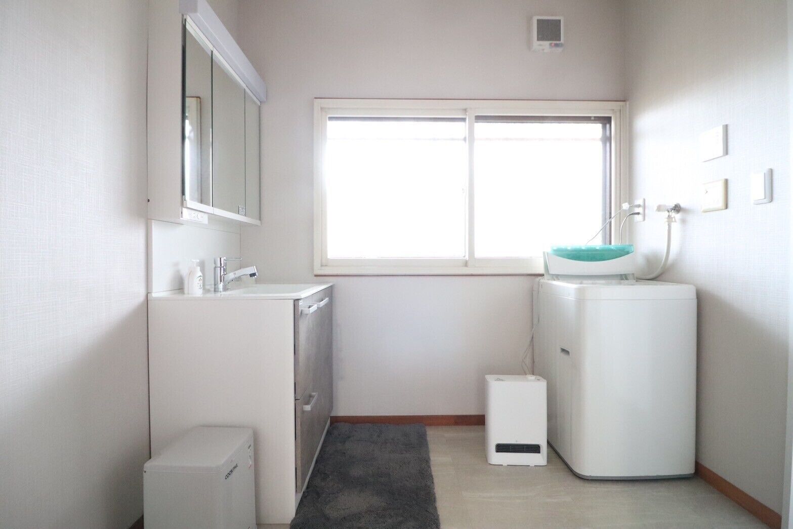 A small, bright bathroom with a window, a sink, a mirror, and a compact washing machine.