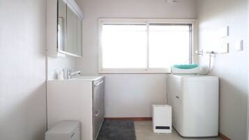 A small, bright bathroom with a window, a sink, a mirror, and a compact washing machine.