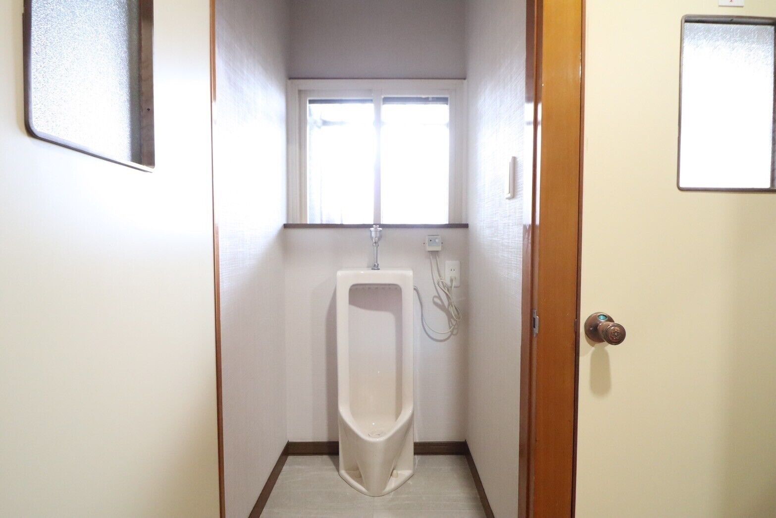 A small, narrow bathroom with a urinal, a window, and a door.