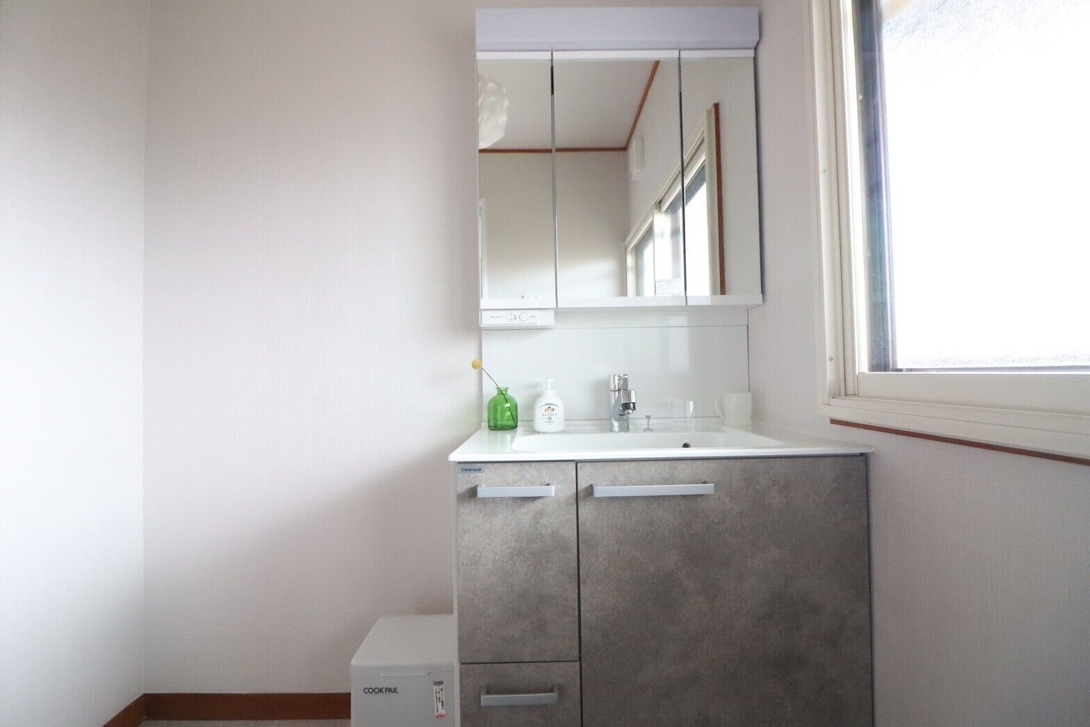 A bathroom with a white sink, a mirror above it, and a window to the right.