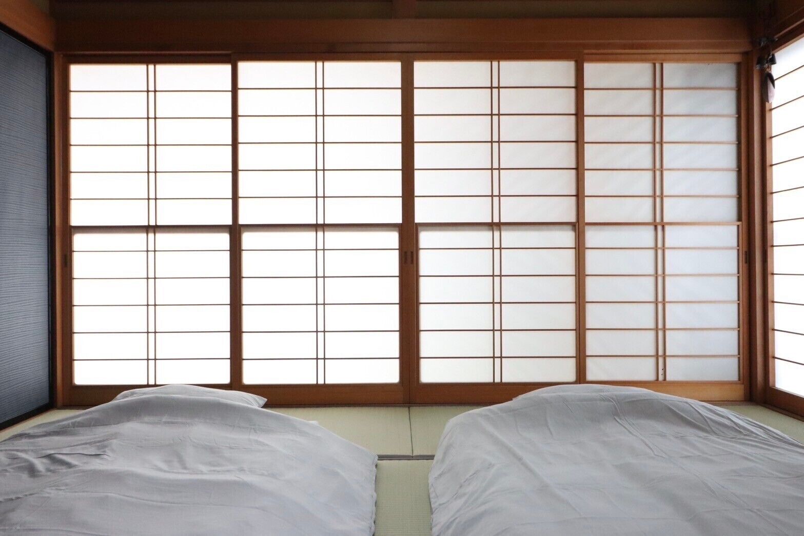 Een traditionele Japanse kamer met tatami vloeren, een shoji schuifdeur en twee bedden met witte beddengoed.