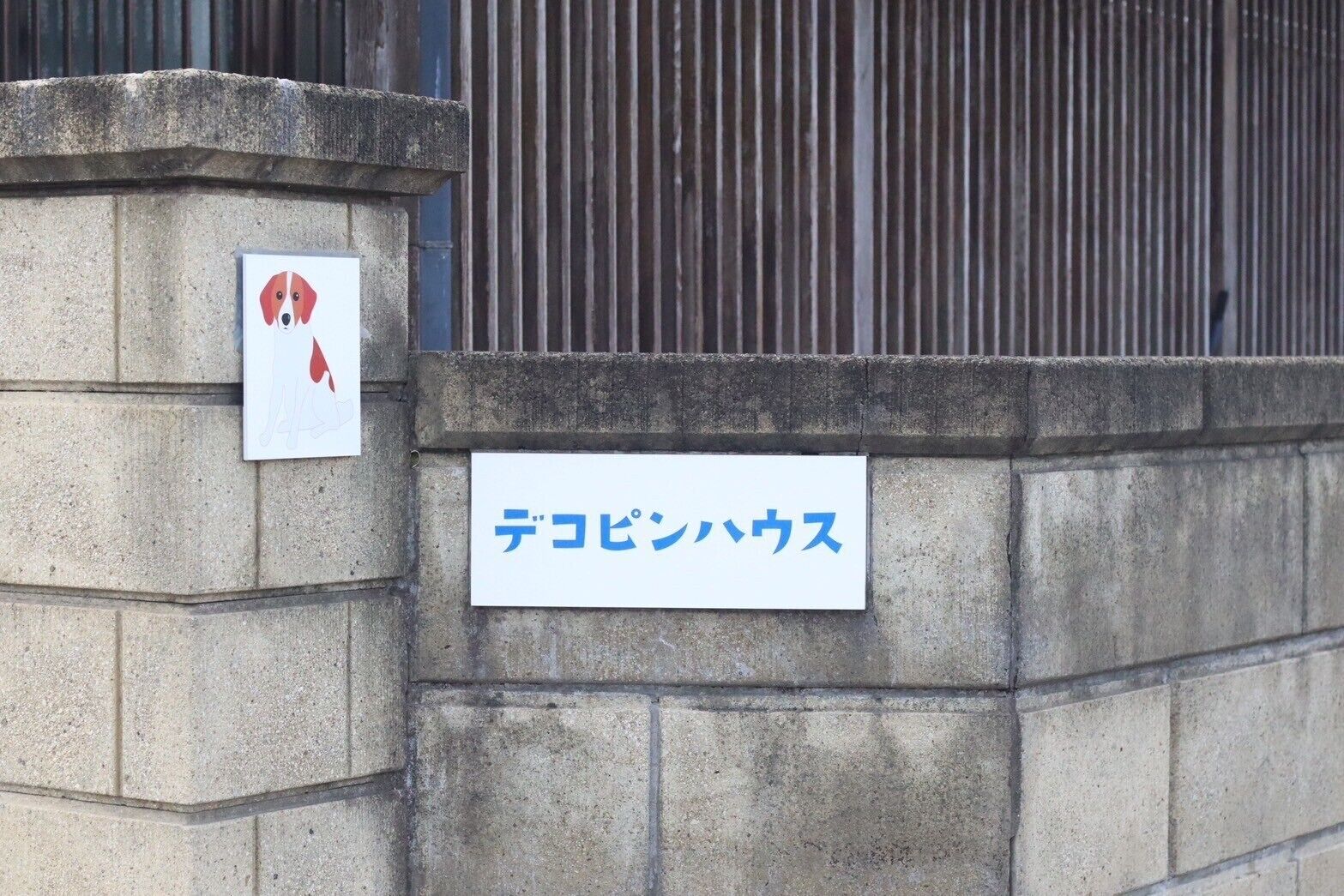 A stone wall with a sign that reads "Dejima Hokusai" and a small sign with a red dog illustration.