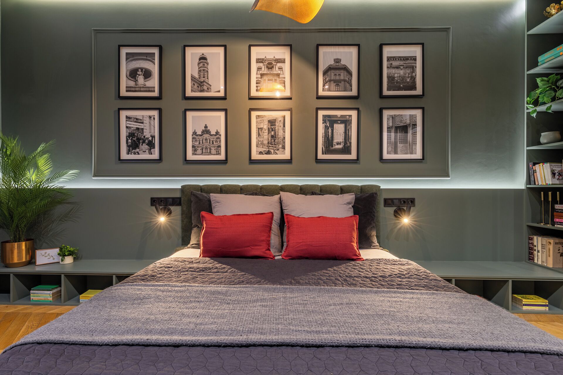 A modern bedroom with a large bed, a headboard with built-in lighting, a wall-mounted bookshelf, and a series of framed black and white photographs.
