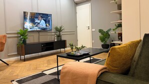 Ein modernes Wohnzimmer mit Flachbildfernseher, einer Couch, einem Couchtisch und Zimmerpflanzen.
