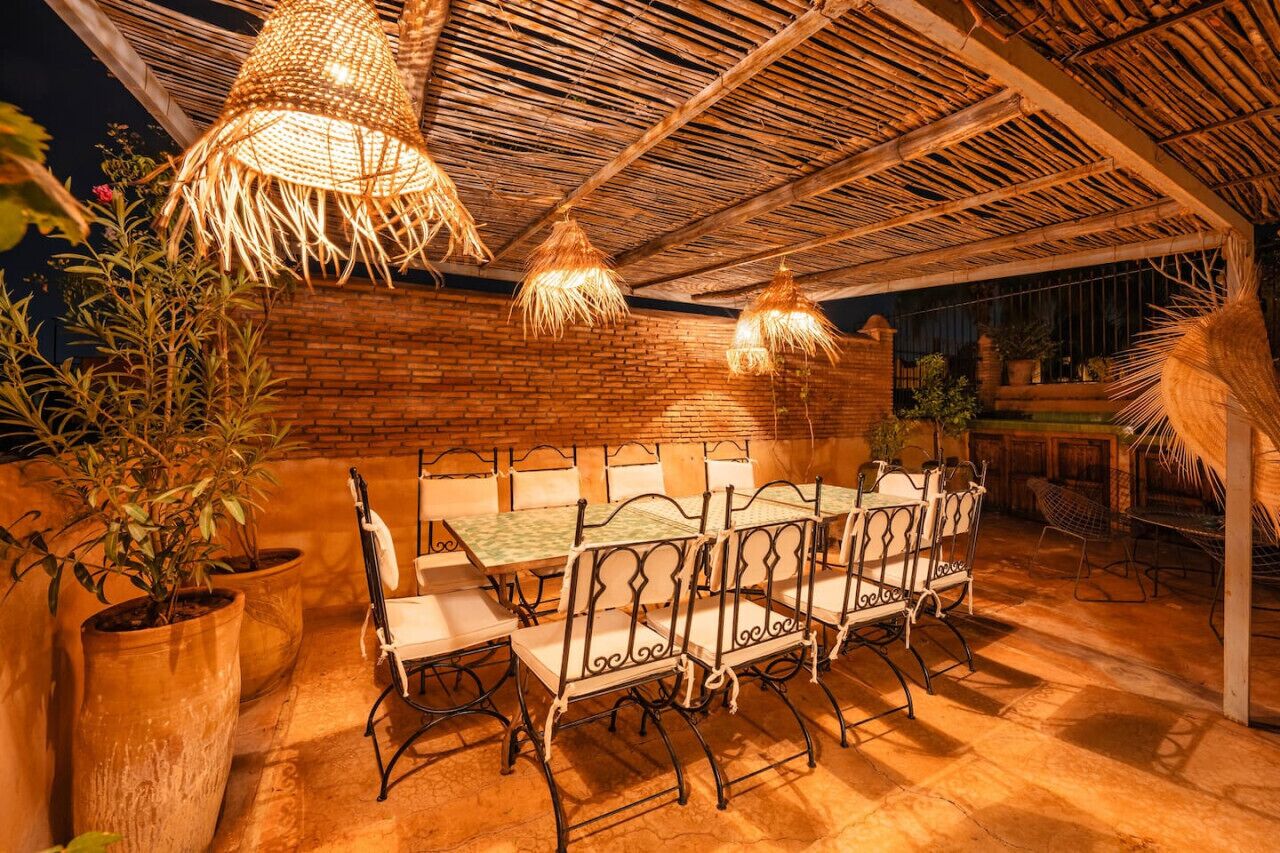 An outdoor dining area with a brick wall, thatched ceiling, and hanging lights.