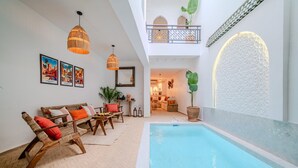 Un vaste espace intérieur abritant une piscine, offrant une vue dégagée sur celle-ci, un coin salon avec des meubles en osier et un balcon agrémenté de balustrades décoratives.